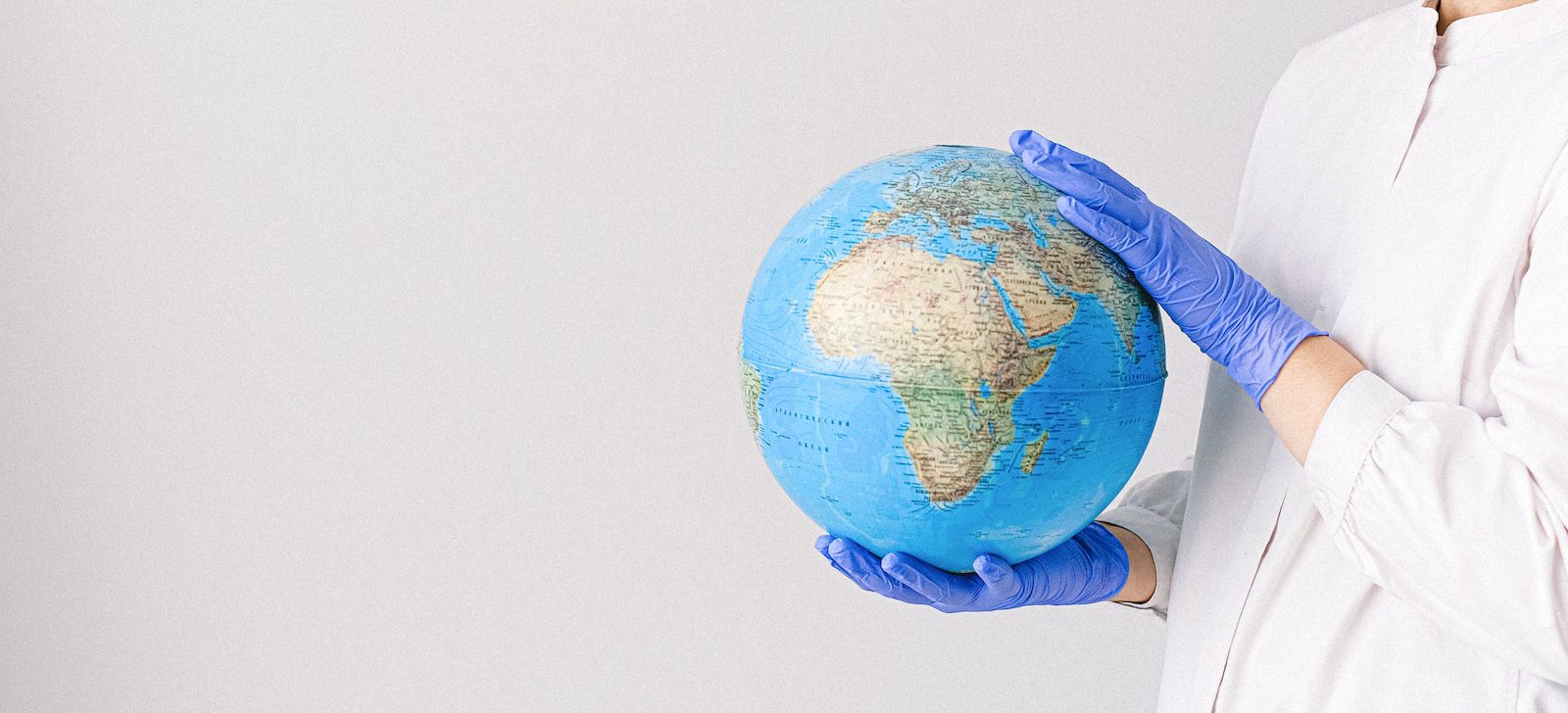 Person With a Face Mask and Latex Gloves Holding a Globe