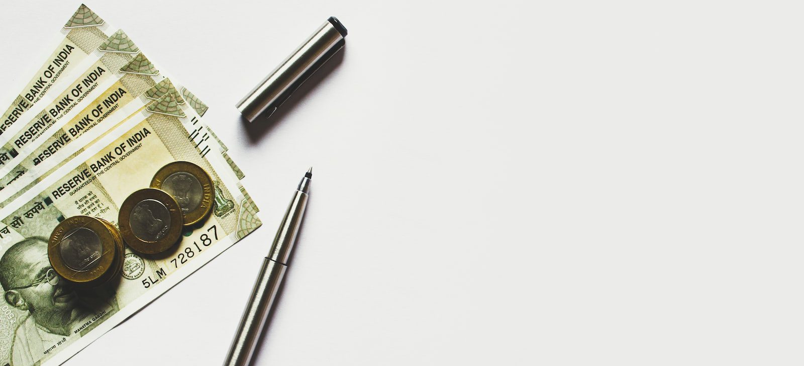 gray pen beside coins on Indian rupee banknotes